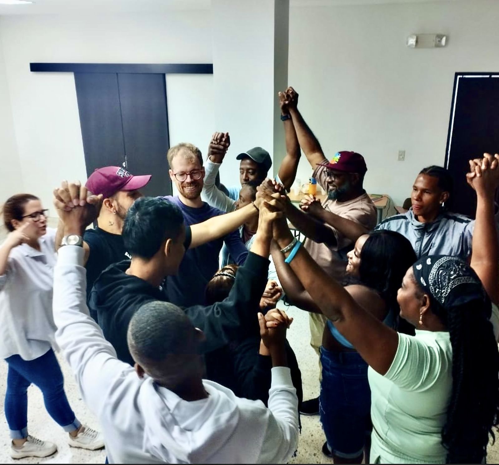Program participants and facilitators in Cali standing in a circle, hands raised and joined together